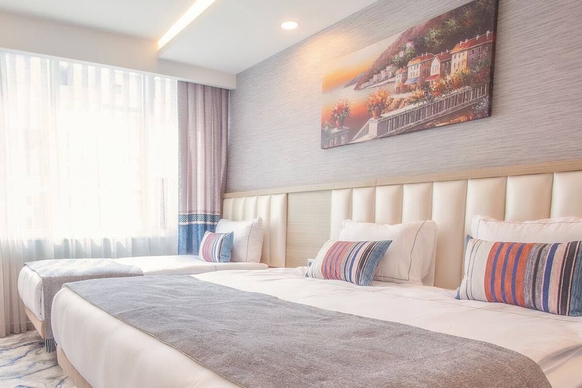 A hotel room with two beds, a large painting on the wall, and a view of a building through the window.