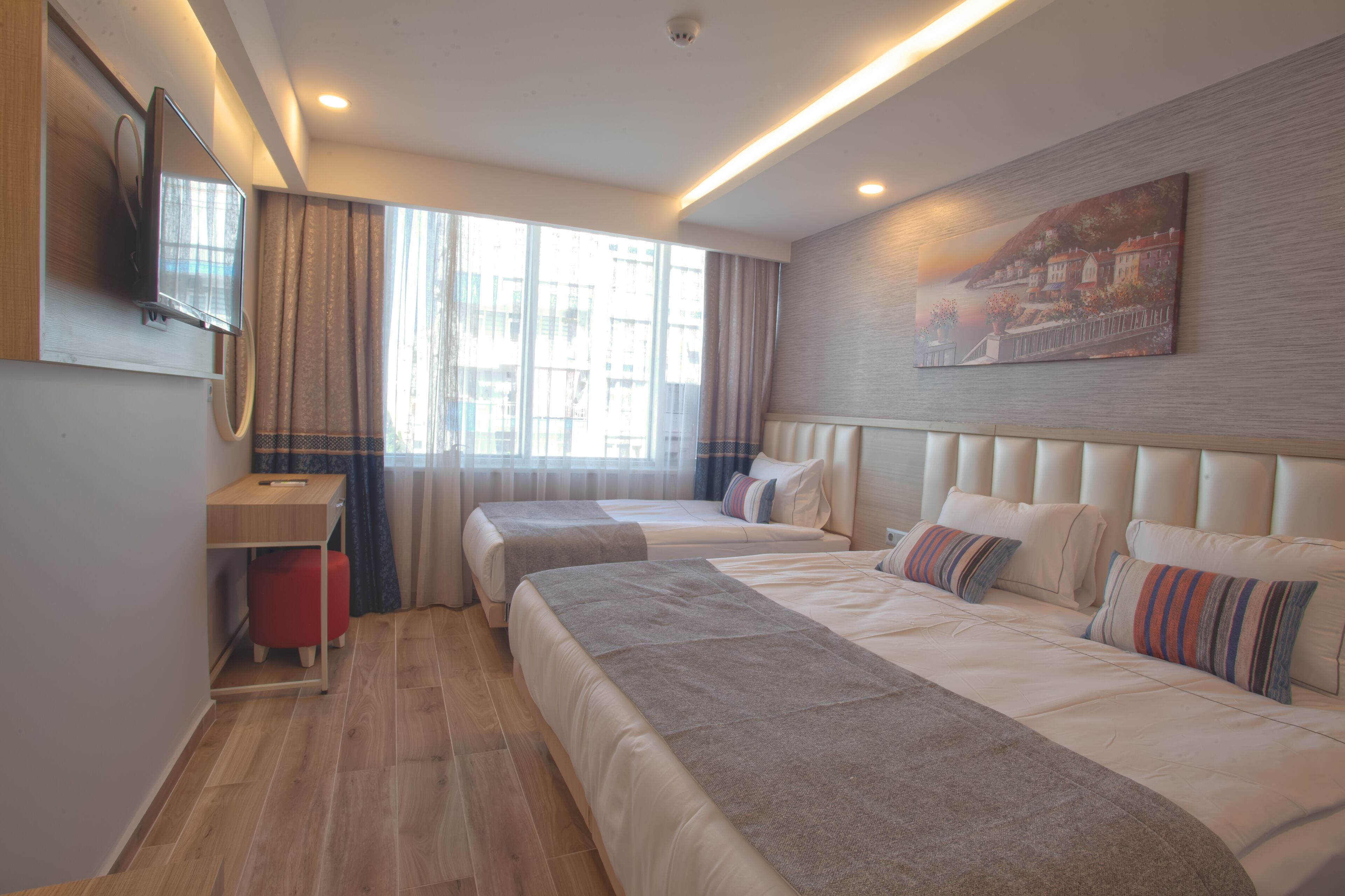 Ein Hotelzimmer mit zwei Betten, einem Schreibtisch, einem Fernseher und einem Gemälde an der Wand.