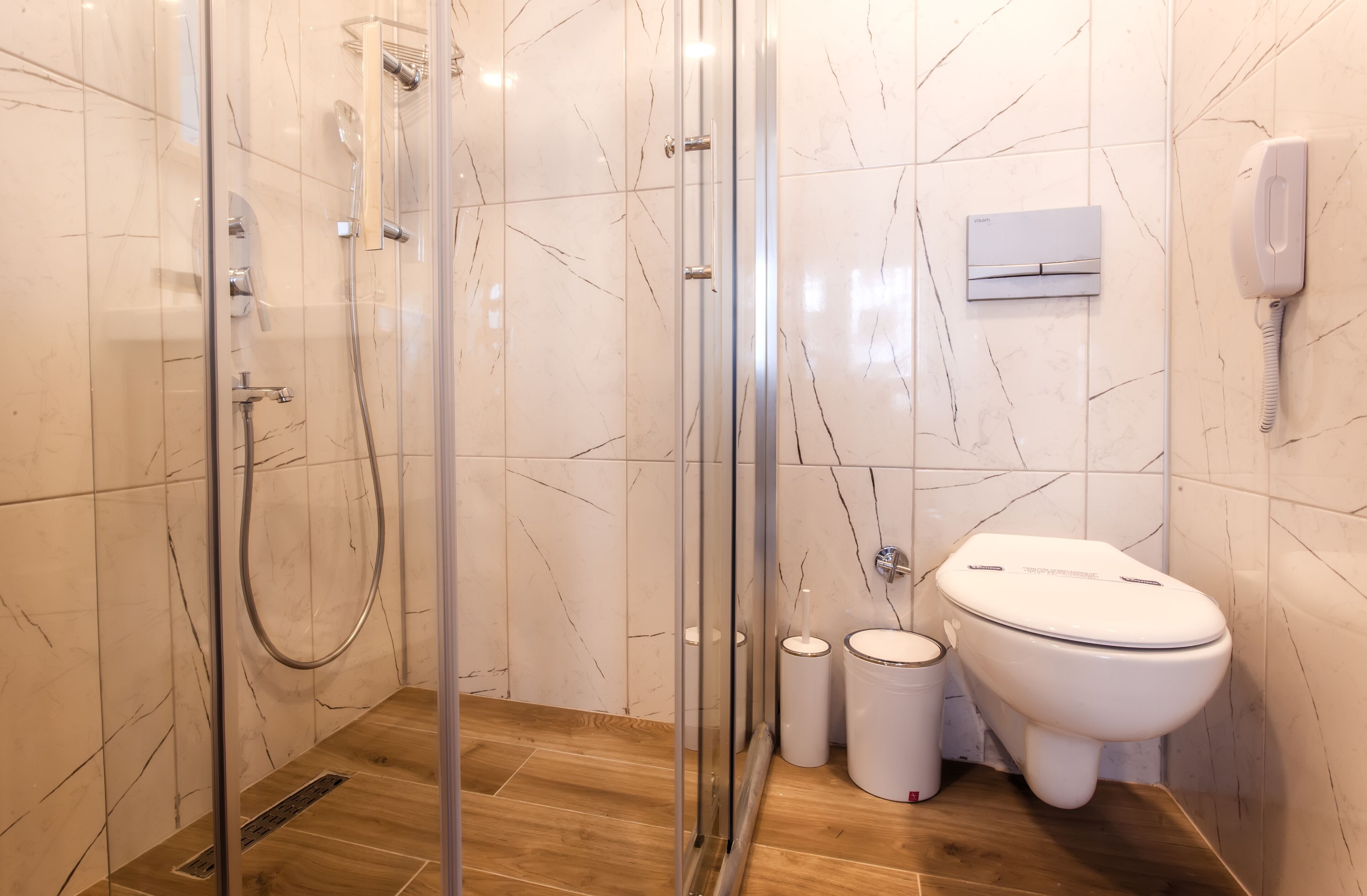A modern bathroom with a glass-enclosed shower, a toilet, and a wall-mounted phone.