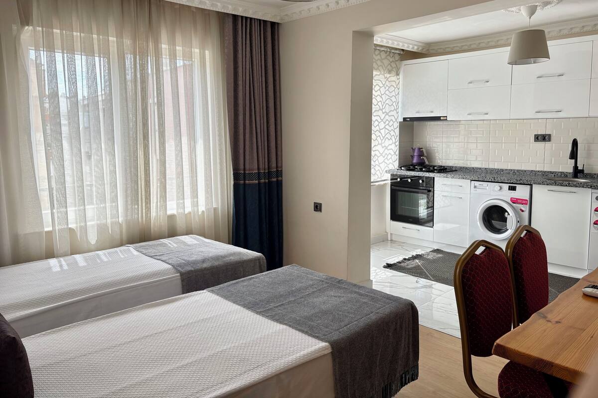 A hotel room with two beds, a dining table, and a kitchen area with appliances.