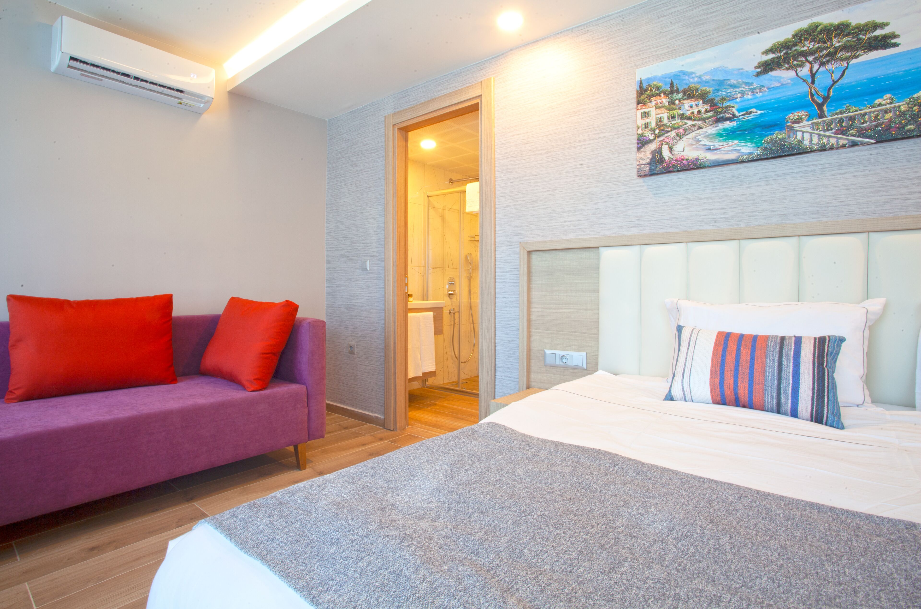 A hotel room with a bed, a sofa, and a painting of a coastal scene.
