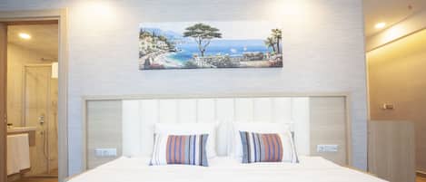 A bedroom with a large bed, a painting of a coastal scene, and a bathroom visible through an open door.