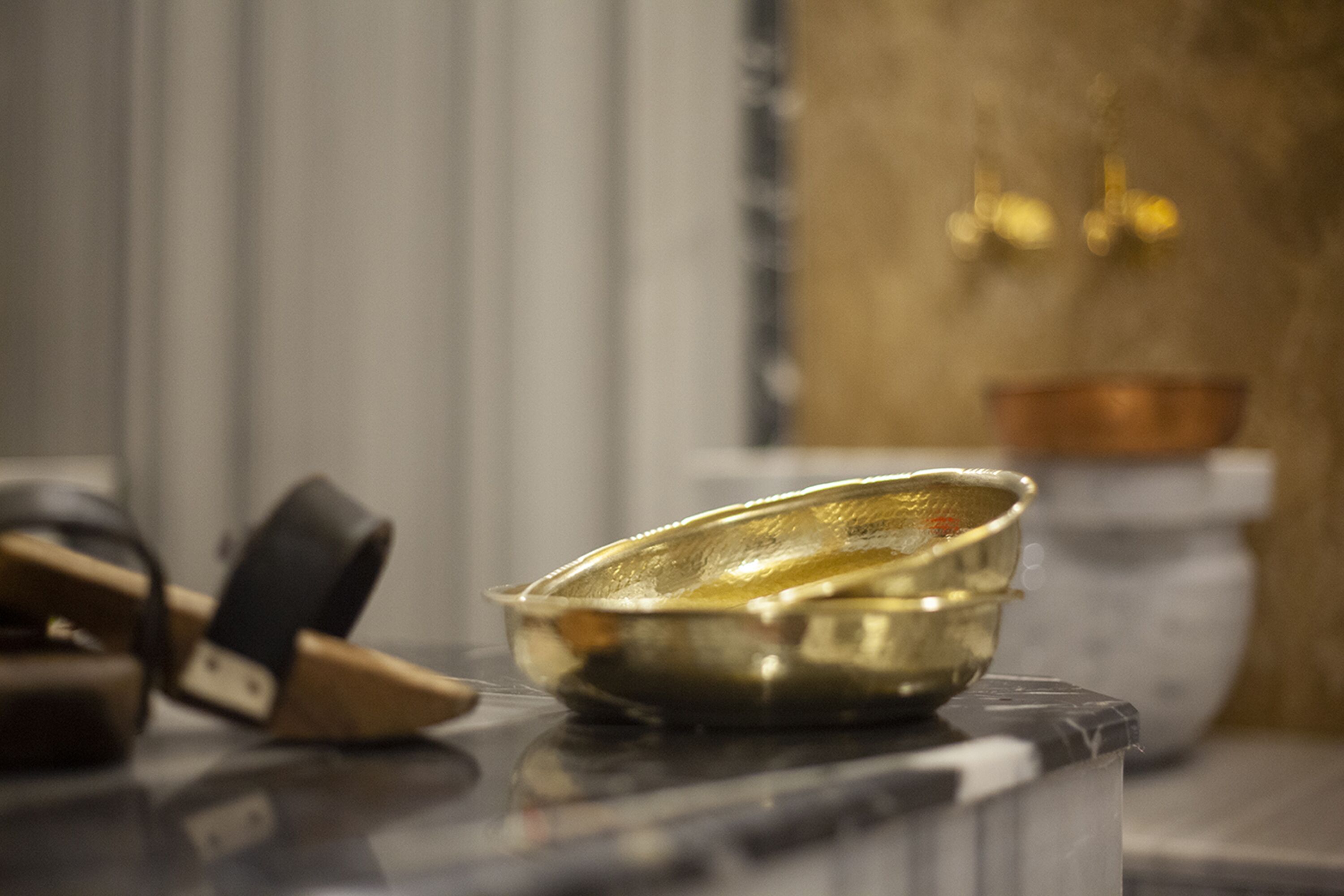 A brass bowl on a marble surface, a black and beige belt, and a blurred background with a golden object.