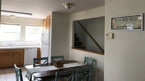 A dining area with a table and chairs, a kitchen with wooden cabinets, a refrigerator, and a staircase.