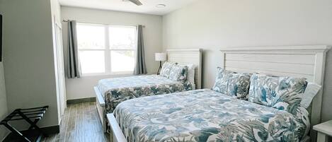A bedroom with two beds, a ceiling fan, a window with curtains, and a wooden floor.