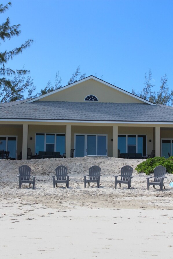 Un bâtiment situé en bord de mer, doté d’un toit plat, de grandes fenêtres et d’un espace abrité avec des chaises de plage.