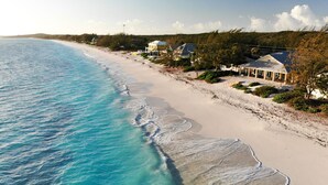 Une propriété située sur la côte, offrant une vue sur la plage, avec une plage de sable et une rangée de maisons dotées de grandes fenêtres.