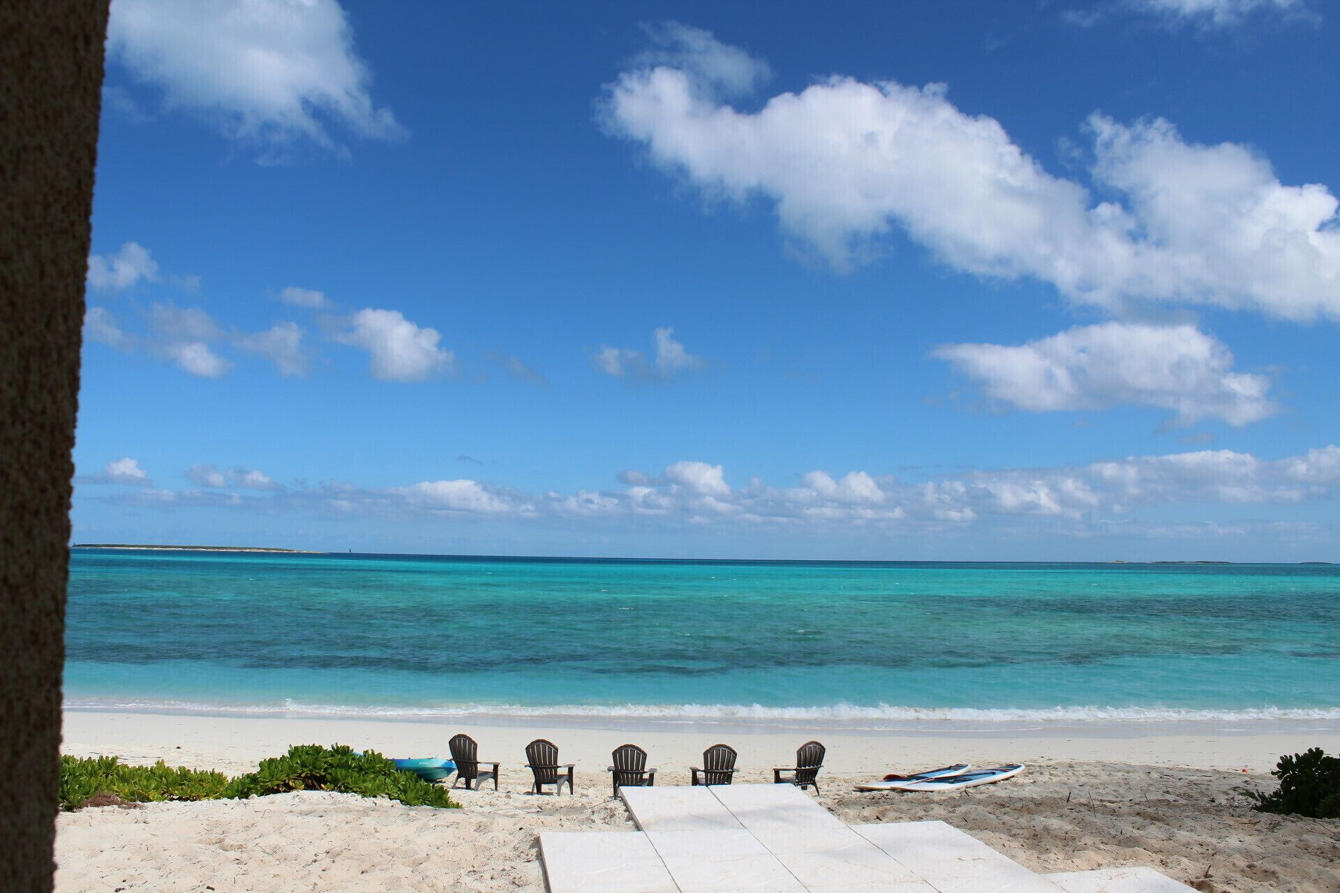 A beach with a row of chairs facing the ocean, a surfboard, and a clear blue sky.