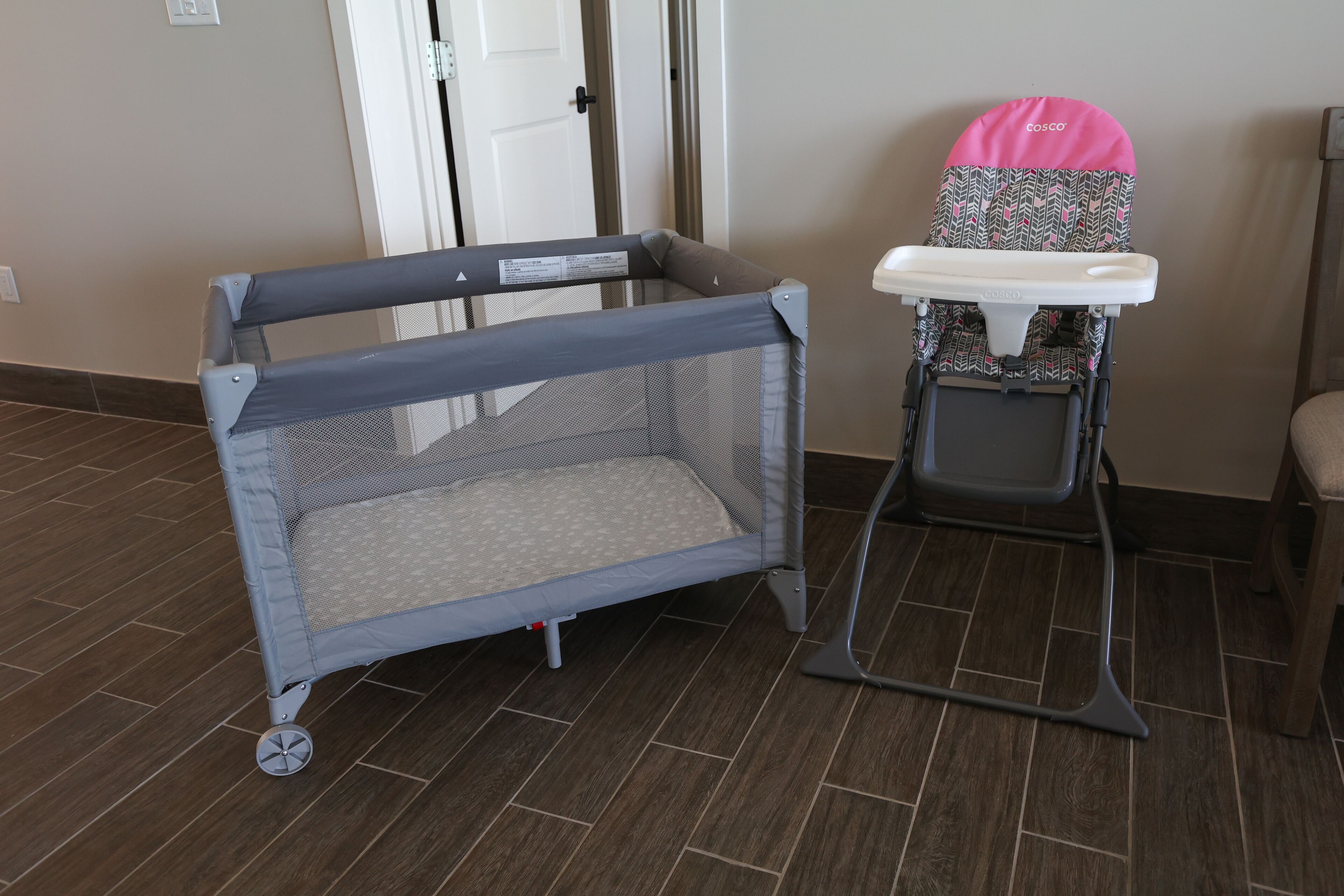 A baby playpen with wheels and a high chair with a patterned cover.