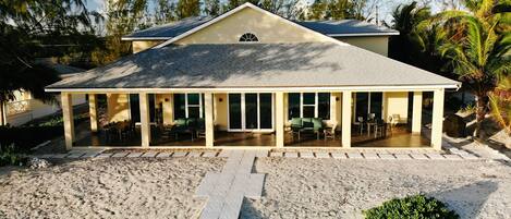 A beach house with a covered patio, a wooden deck, and a sandy beach area.