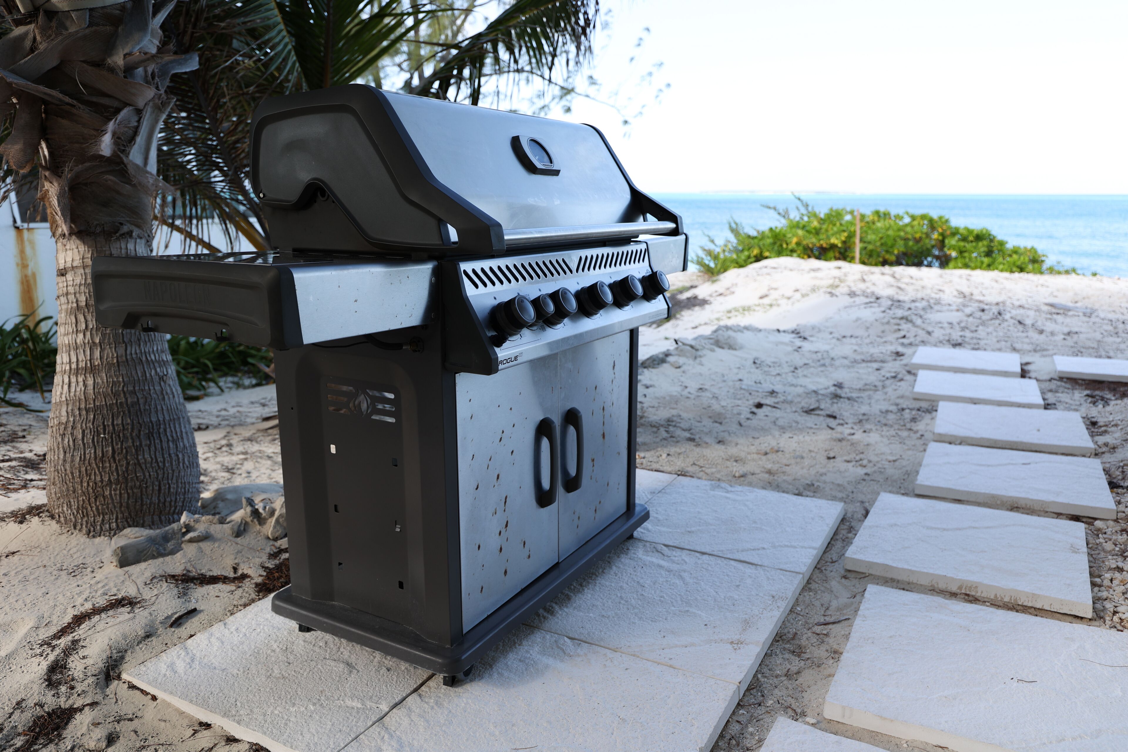 A portable grill on a sandy surface with a view of the ocean in the background.