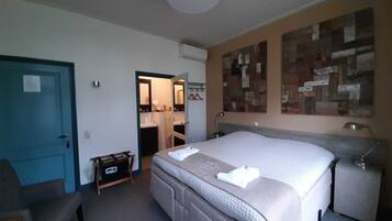 Een slaapkamer met een bed, nachtkastje, stoel, kast en een zichtbare badkamer door een geopende deur.