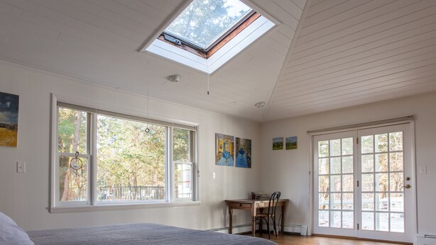 Ein Schlafzimmer mit Dachfenster, großen Fenstern und Blick auf Bäume.