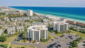 A coastal hotel with modern architecture, a parking lot, and a view of the beach. - Adorable 2BD 2BA- Walk to Beach-Enclave  Condos! (Destin)