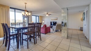 A spacious living area with a dining table, chairs, a red sofa, a TV, and a ceiling fan. - Adorable 2BD 2BA- Walk to Beach-Enclave  Condos! (Destin)