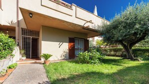 A house with a paved entrance, a small garden with potted plants, and a large tree.