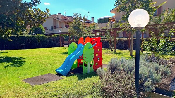 Ein Spielplatz mit Rutschen und Klettergerüsten, umgeben von einem gepflegten Rasen und Hecken.