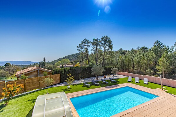 Une piscine offrant une vue sur une forêt et des collines en arrière-plan.