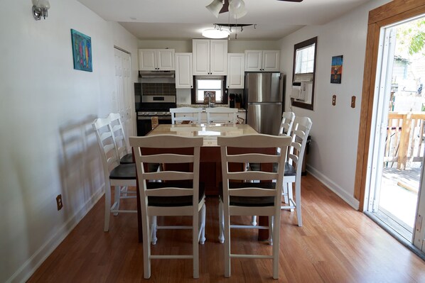 A modern kitchen with white cabinets, a stainless steel refrigerator, and a central island with chairs. - Quiet Conch House in Historic District (Key West)