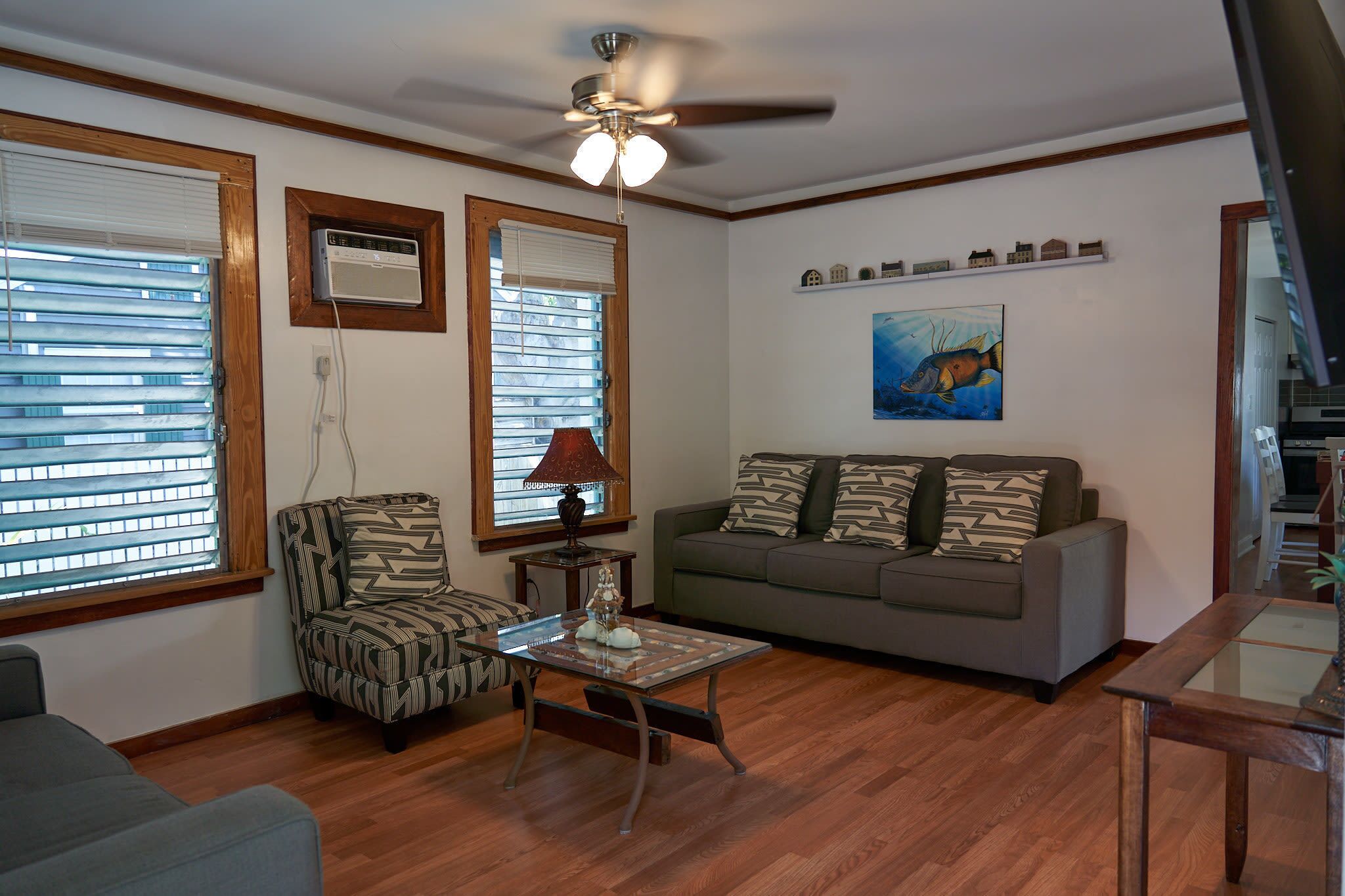 A living room with a ceiling fan, a sofa, a patterned armchair, a coffee table, and a painting on the wall.