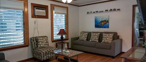 A living room with a ceiling fan, a sofa, a patterned armchair, a coffee table, and a painting on the wall.
