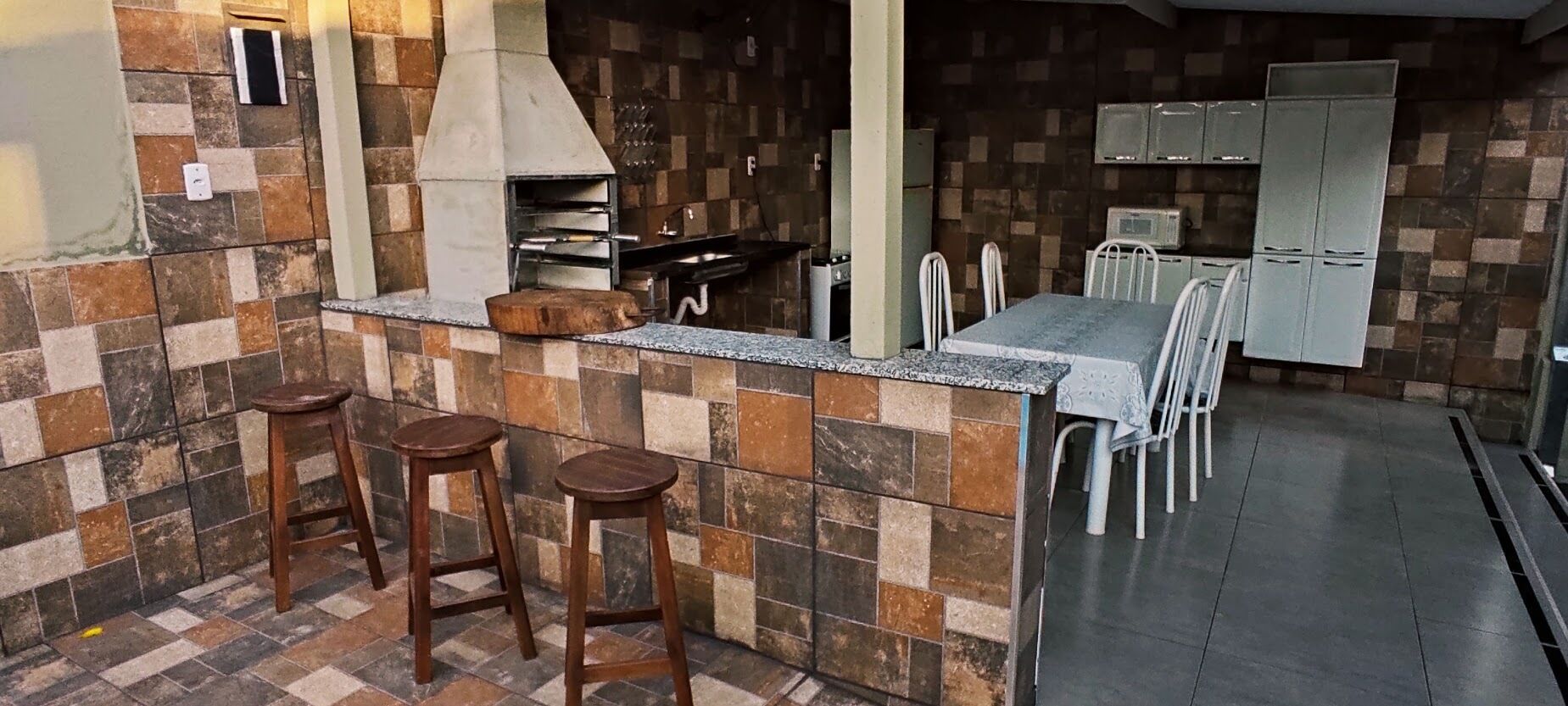 Une cuisine avec un mur recouvert de carreaux, un four encastré, des tabourets de bar, une table à manger avec des chaises et un réfrigérateur.