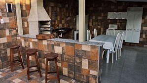 Une cuisine avec un mur recouvert de carreaux, un four encastré, des tabourets de bar, une table à manger avec des chaises et un réfrigérateur.