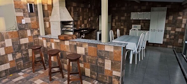 A kitchen with a tiled backsplash, a built-in oven, bar stools, a dining table with chairs, and a refrigerator. - Heated pool, air conditioning, Wi-Fi, 3 minutes from the park (SP)