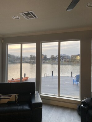 A room with large windows overlooking a dock and water, a black leather sofa, and a blue chair. - Amazing lake spot across from #12 Applerock tee box! (Horseshoe Bay)