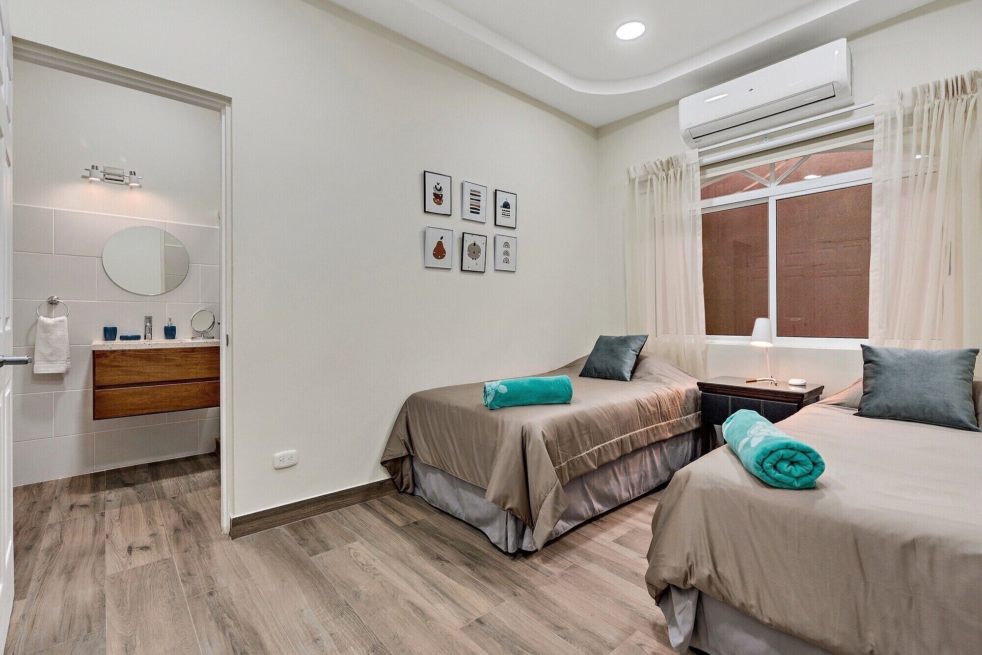 A bedroom with two beds, a bathroom with a mirror and sink, and a window with curtains.