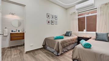 A bedroom with two beds, a bathroom with a mirror and sink, and a window with curtains.