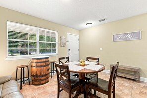 A dining area with a wooden table, chairs, a bar stool, and a window with blinds.