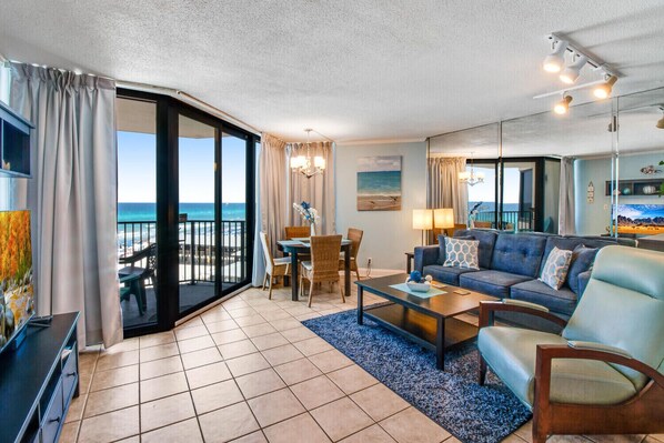 A spacious living area with a balcony overlooking the ocean, furnished with a sofa, coffee table, and dining set.