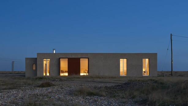 Un bâtiment moderne, de plain-pied, doté de grandes fenêtres et d’une porte ouverte, situé dans un paysage rural.