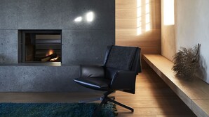 Un salon moderne avec une cheminée, un fauteuil en cuir noir, un plancher en bois et un mur en béton.