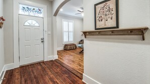 Ein Korridor mit einer weißen Tür, Holzboden, einem Deckenventilator und einem gerahmten Bild an der Wand.
