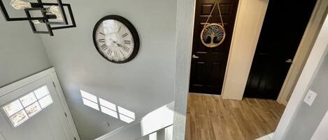 Una escalera con barandilla blanca, un reloj de pared y una lámpara colgante.