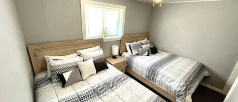 A bedroom with two beds, a ceiling fan, a window, and a nightstand with a lamp.