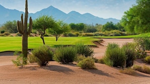A desert landscape with a cactus, trees, and a golf course.