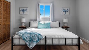 Une chambre à coucher comprenant un lit, deux tables de chevet, une fenêtre avec des rideaux et deux œuvres d’art accrochées au mur.