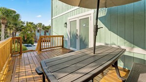 Une terrasse en bois avec une table et un parasol, une porte, et une piscine en arrière-plan.