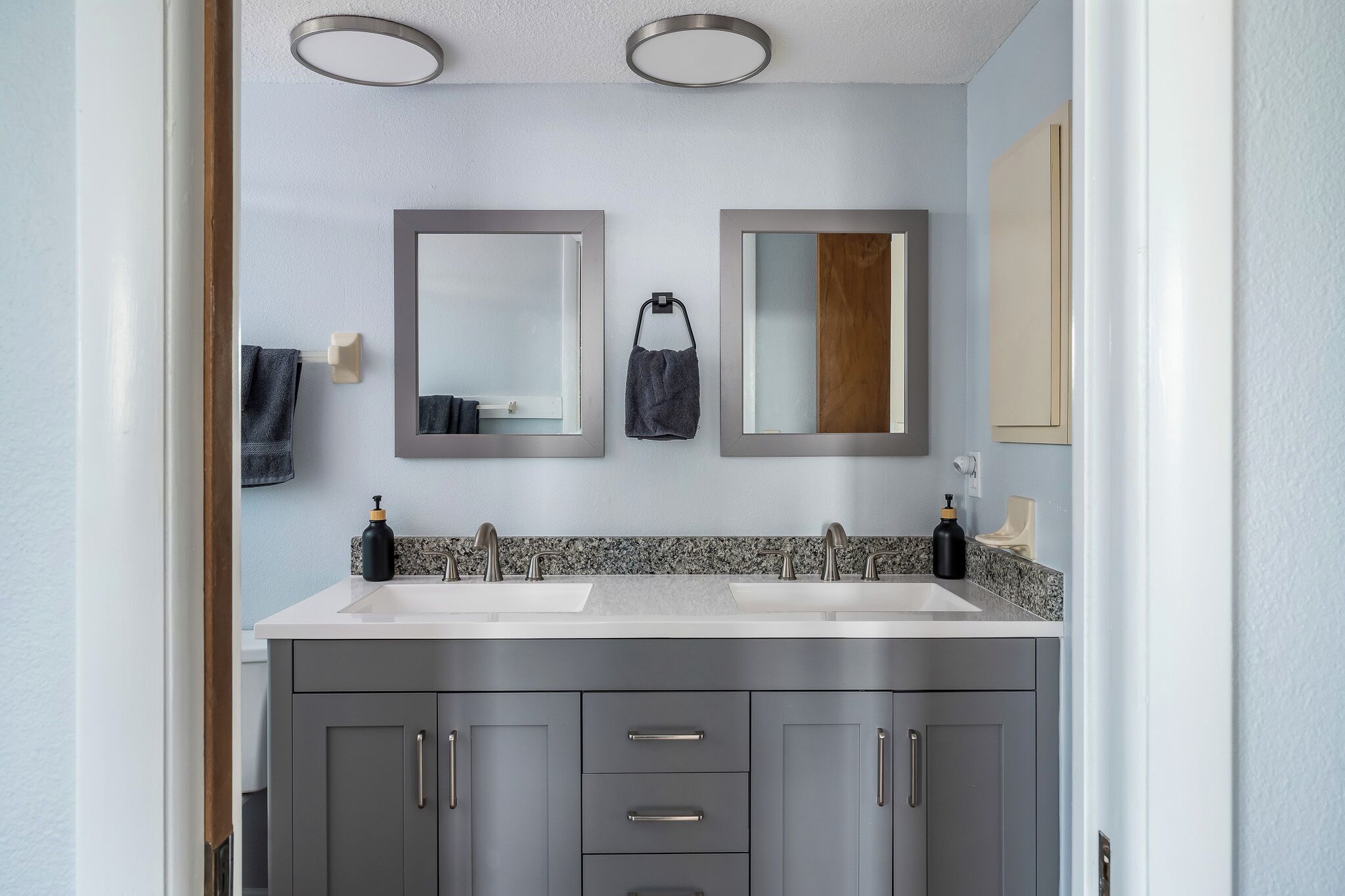 A modern bathroom with two sinks, a large mirror, and a granite countertop.