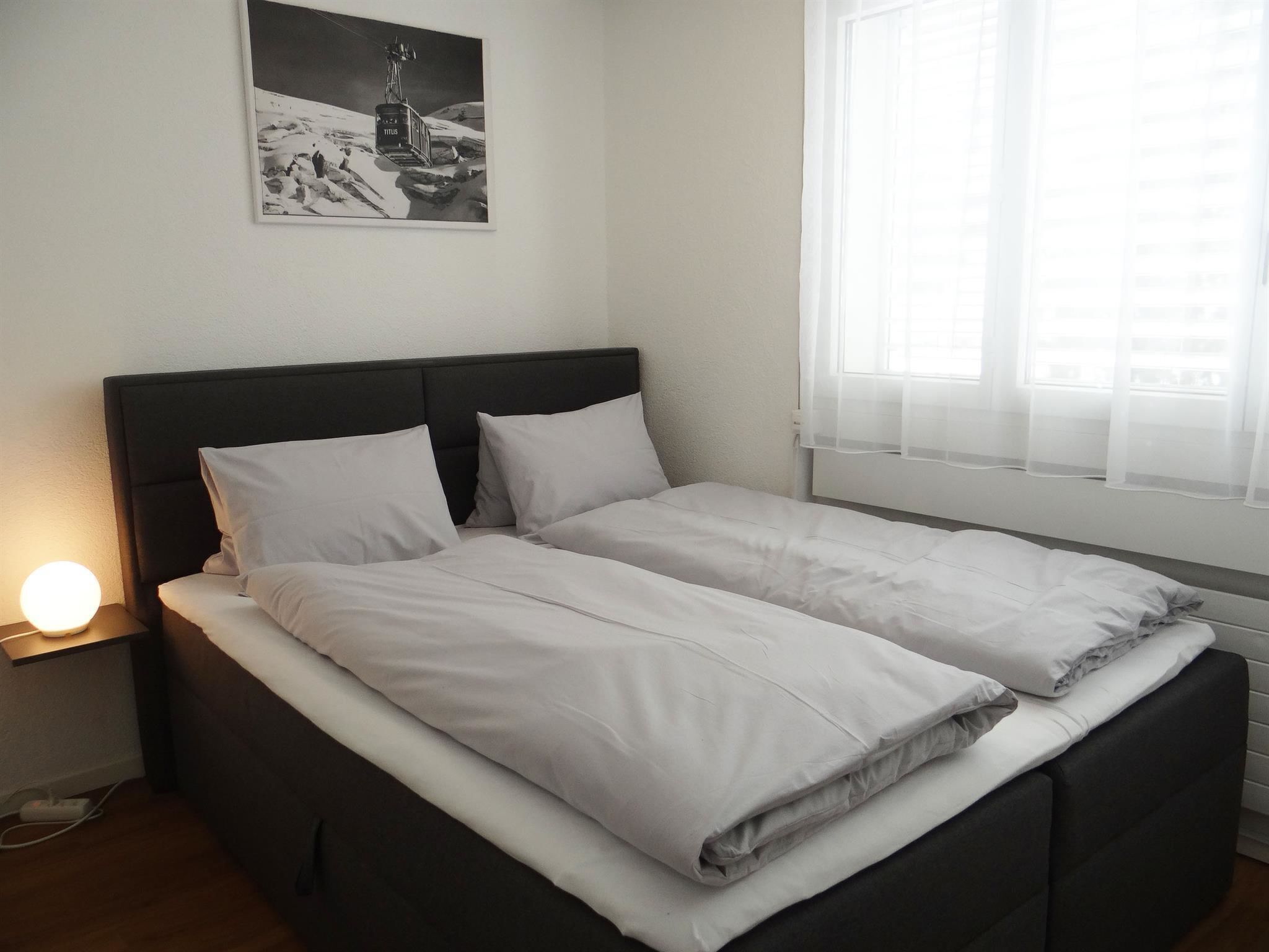 A double bed with white bedding in a room with a window and a wall-mounted picture.