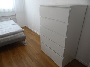 A bedroom with a bed, a wooden floor, and a white wardrobe.