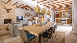 A spacious living area with a stone wall, a wooden dining table, and a modern kitchen in the background. - Xarabella - Denia, Costa Blanca (Denia)