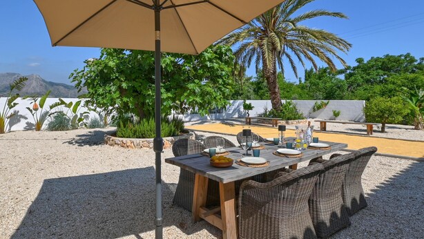 An outdoor dining area with a table set for four, surrounded by wicker chairs, under a large umbrella.