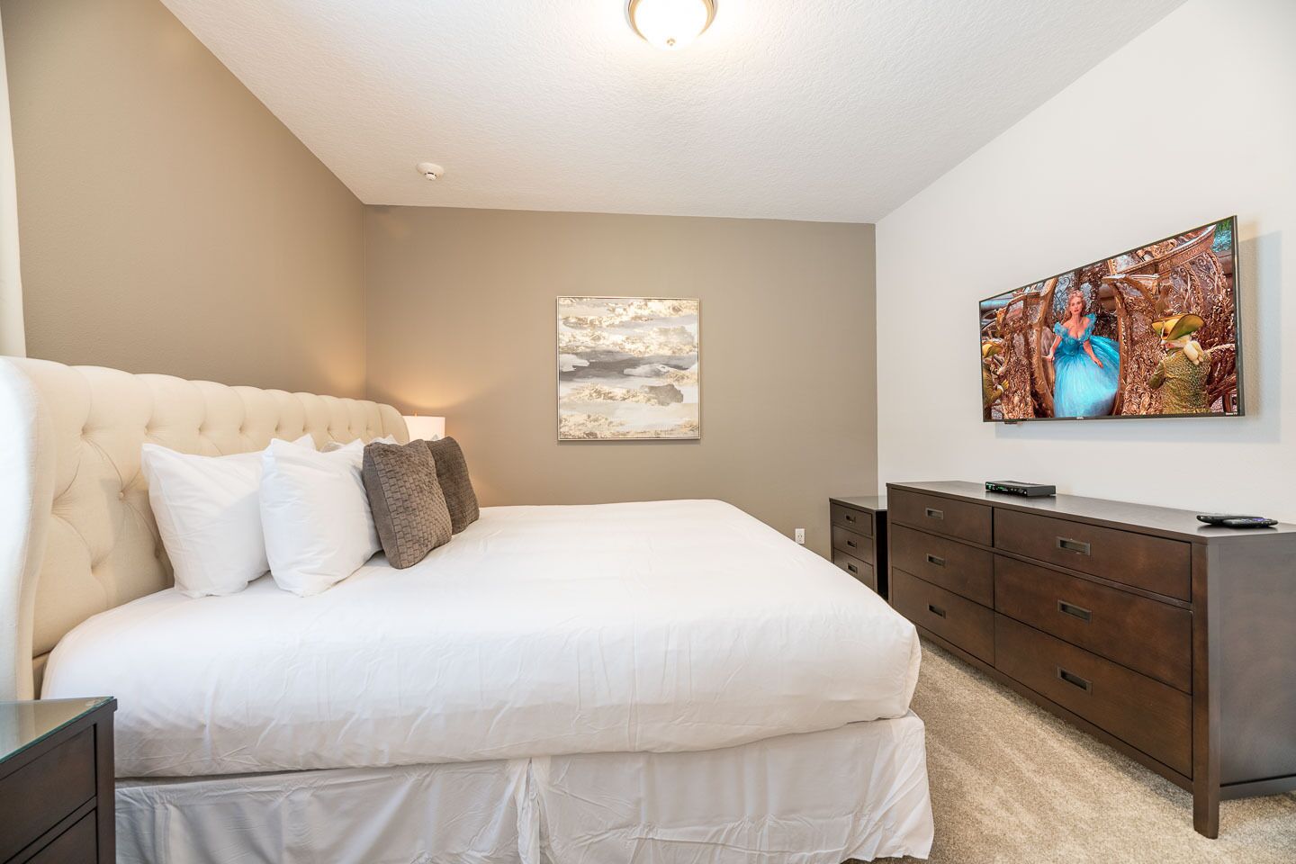 A bedroom with a large bed, a dresser, a flat-screen TV, and a framed picture on the wall.