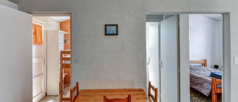 Een kamer met een houten eettafel en stoelen, een klein, ingelijst beeldje aan de muur, en een bed met een houten hoofdbord in de aangrenzende ruimte.