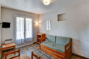 A small, cozy room with a checkered sofa, a wooden table, a TV mounted on the wall, and a door leading outside. - Gîte le Chêne Vert in a holiday park (Saint-Savinien)