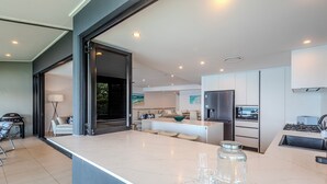 A modern kitchen with a large island, built-in appliances, and a dining area with a sofa and table. - Edge 10 - Magnificent Views! (Hamilton Island)